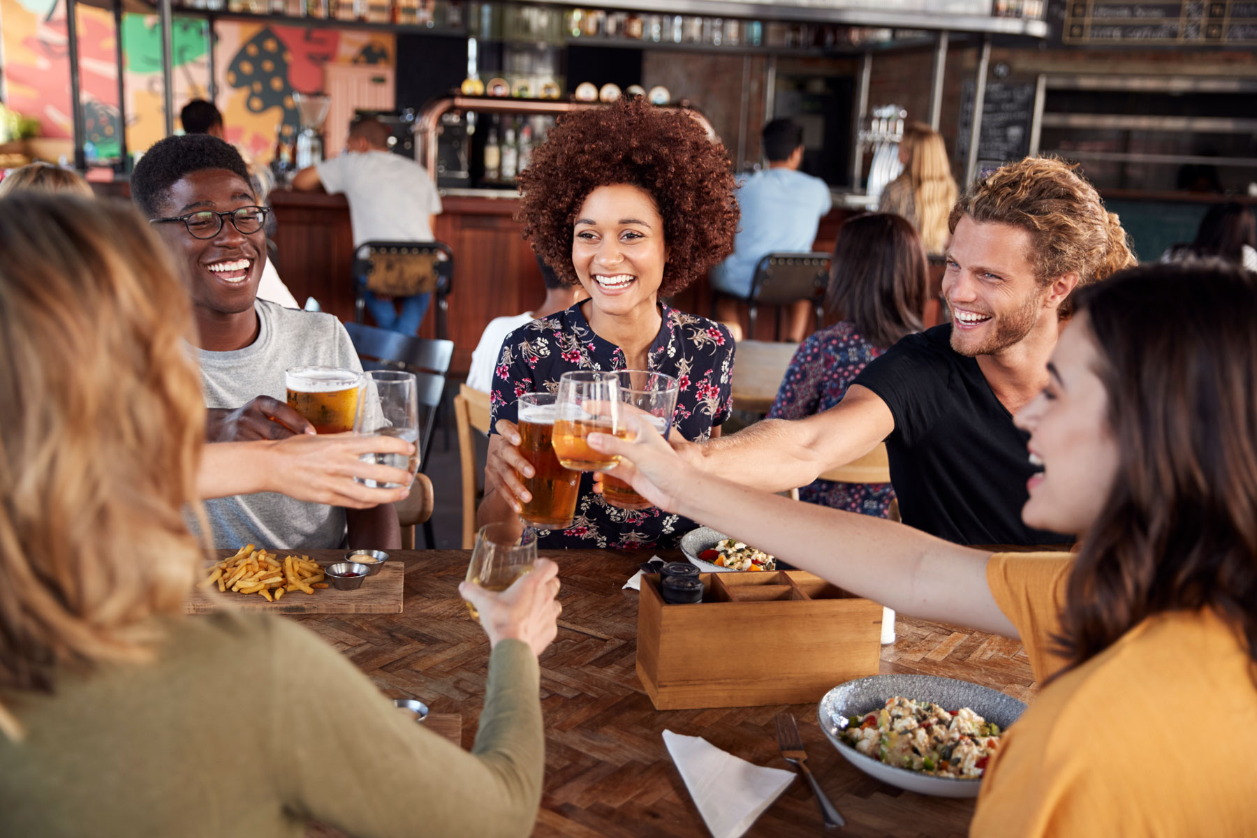 group of diverse young adult friends at local restaurant cheering beers