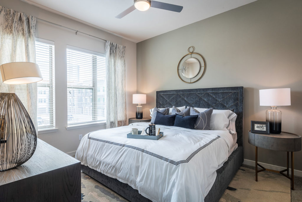 Bedroom with queen size bed, dual nightstands with matching lamps, large windows for natural light, coffee tray on the bed and plush carpeting.