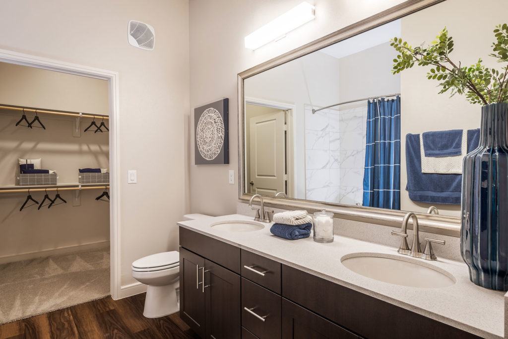 Bathroom with large framed mirror, dual sink vanity, shower/tub combo with curved rod and walk-in closet.