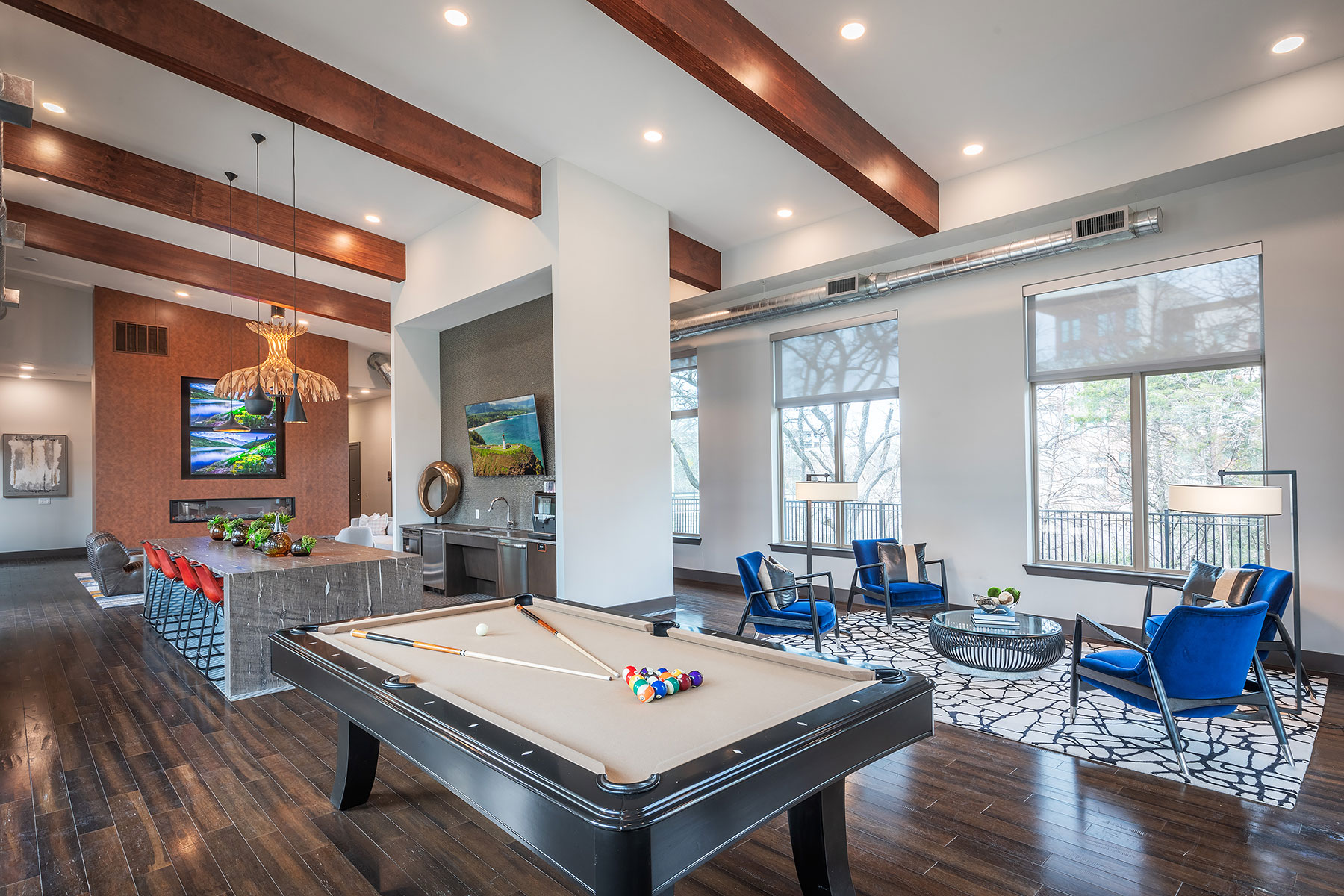 Clubhouse interior with view of bar seating, kitchen area, billiards table and several wall mounted TVs