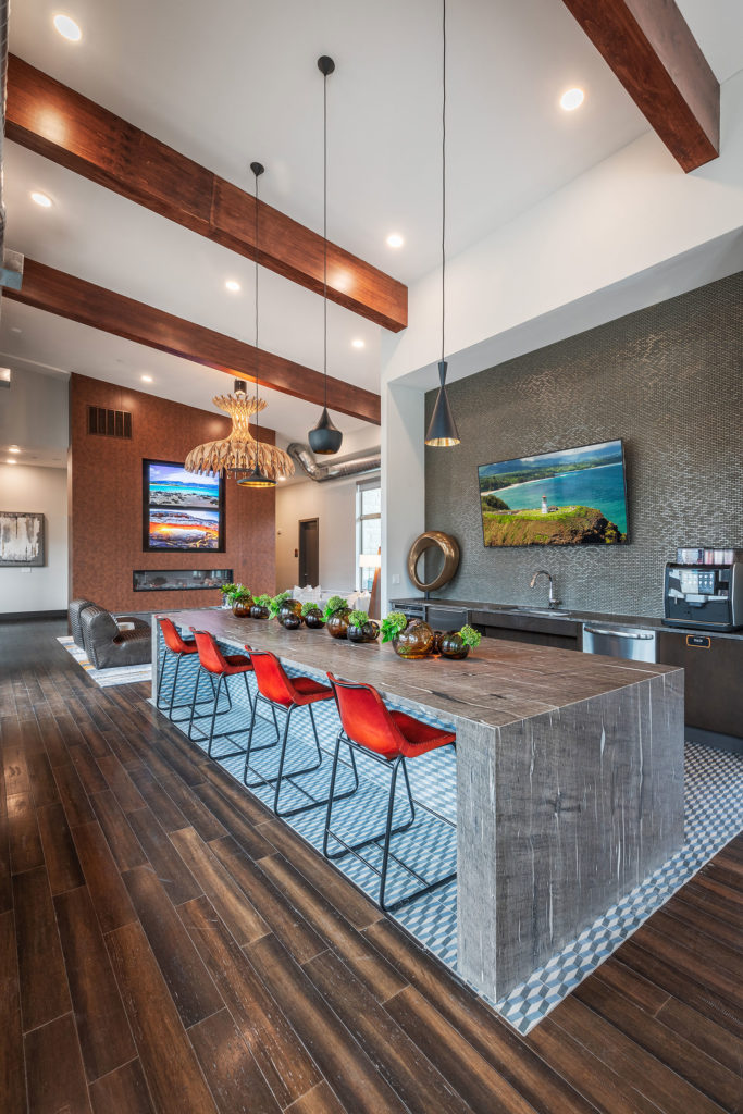 Clubhouse interior with view of bar seating, kitchen area with bar, pendant lighting, wooden floors and several wall mounted TVs