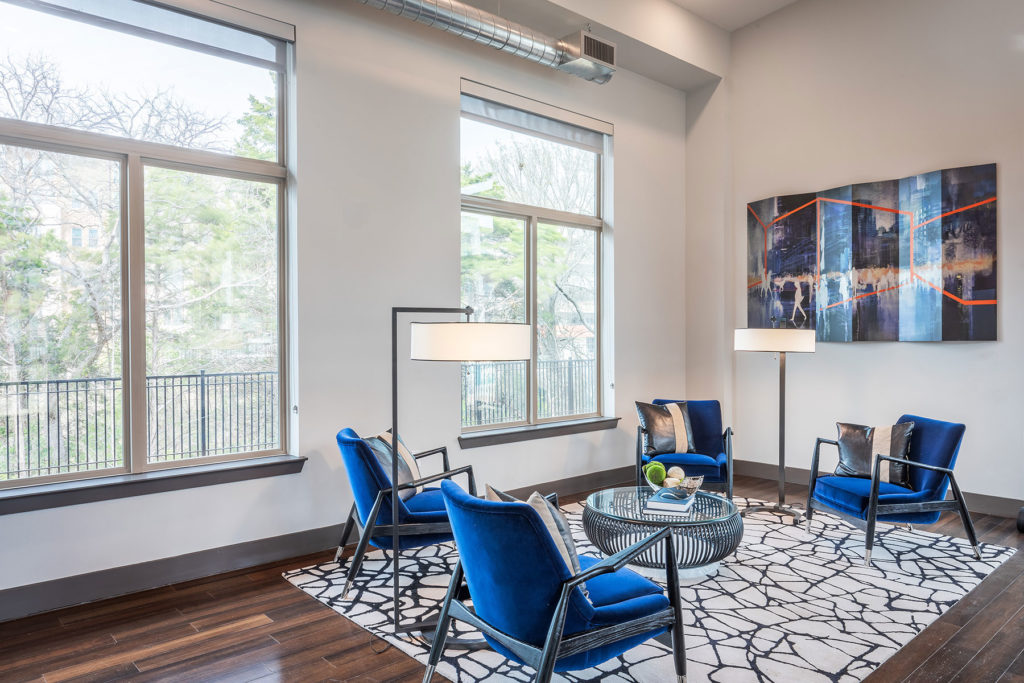 Seating area with contemporary rug, bright blue plush chairs, floor lamps, large windows and sculptural round coffee table.