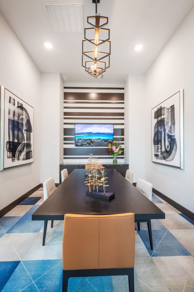 Conference room with colorful geometric rug, long conference desk seating 6, geometric chandelier and contemporary artwork.