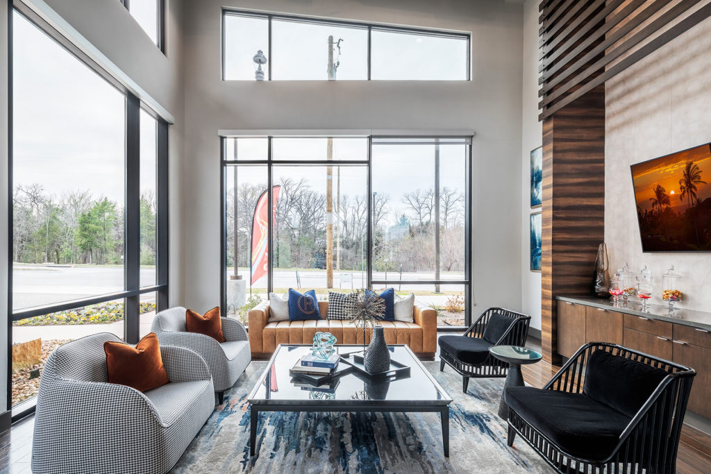 Clubhouse seating area with floor to ceiling windows, plush chairs and couch, glass coffee table, and wall mounted TV.