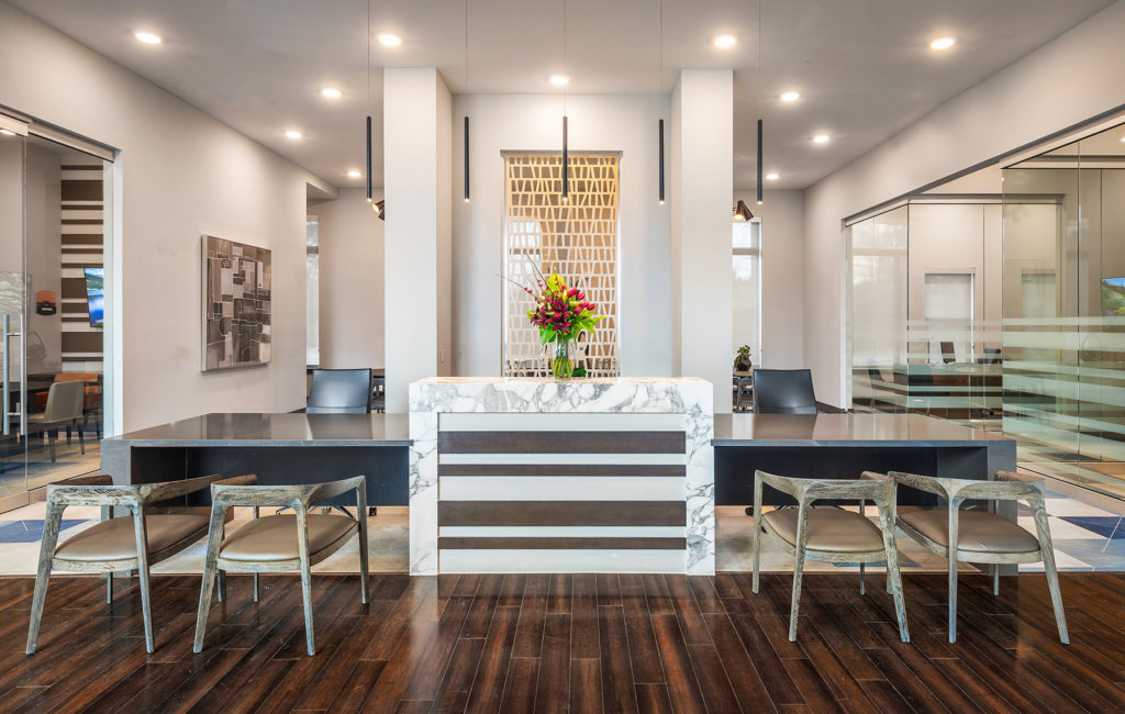 Leasing office concierge desk with modern seating, marble desk with flowers and contemporary hanging artwork.