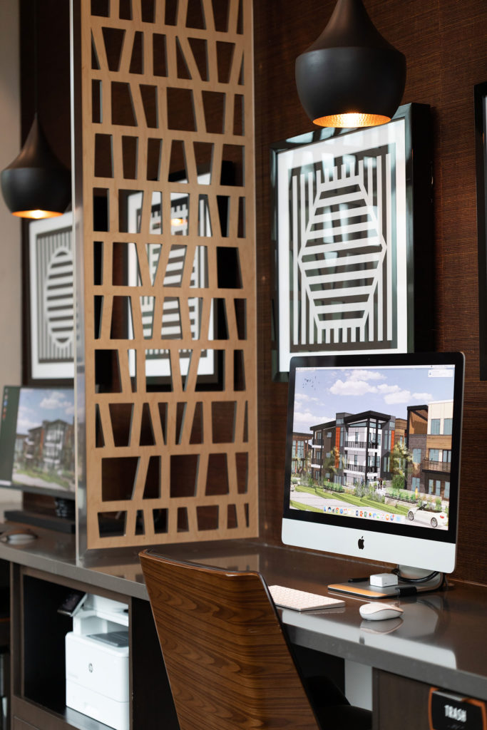 Shot of the business center with a wooden sculptural wall separating the PC and Apple computers, and geometrical artwork on the wall.